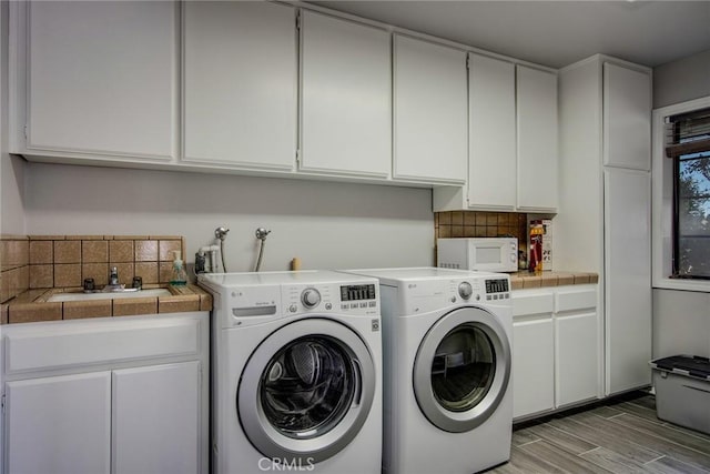 laundry room with sink, washing machine and clothes dryer, light wood-type flooring, and cabinets