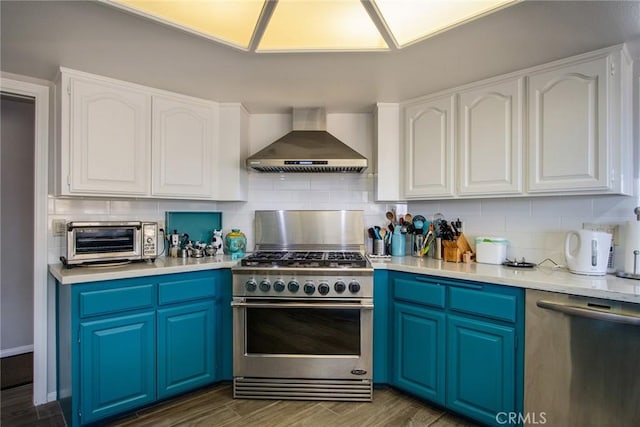 kitchen featuring stainless steel appliances, blue cabinets, tasteful backsplash, white cabinets, and wall chimney exhaust hood