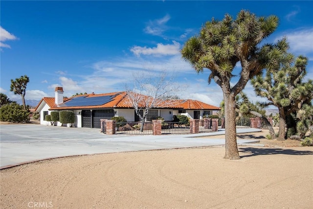 view of front of property with concrete driveway, a fenced front yard, a tile roof, an attached garage, and roof mounted solar panels