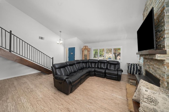 living room with high vaulted ceiling, an inviting chandelier, a fireplace, and light hardwood / wood-style floors