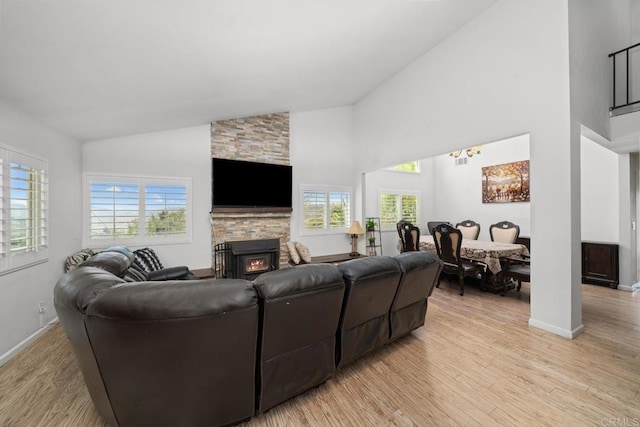 living room with a stone fireplace, high vaulted ceiling, and light hardwood / wood-style flooring