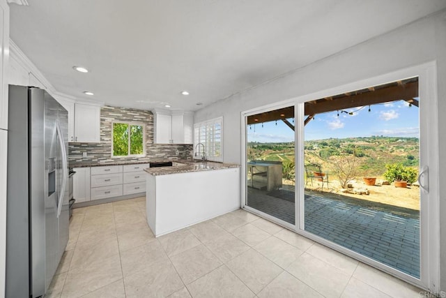 kitchen featuring stainless steel refrigerator with ice dispenser, white cabinetry, dark stone countertops, kitchen peninsula, and backsplash