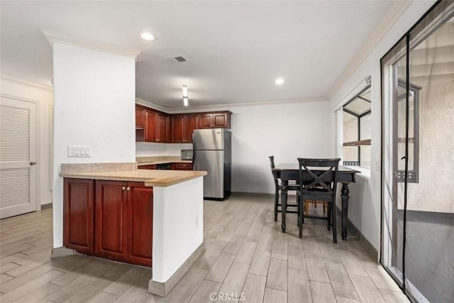 kitchen featuring reddish brown cabinets, wood tiled floor, visible vents, and freestanding refrigerator