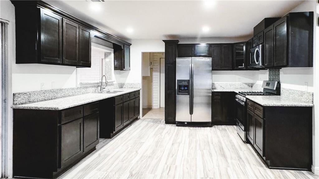 kitchen with light stone counters, sink, light hardwood / wood-style floors, and appliances with stainless steel finishes