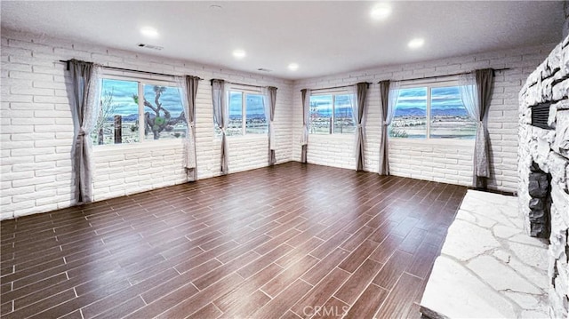 unfurnished living room with a fireplace, dark hardwood / wood-style floors, and brick wall