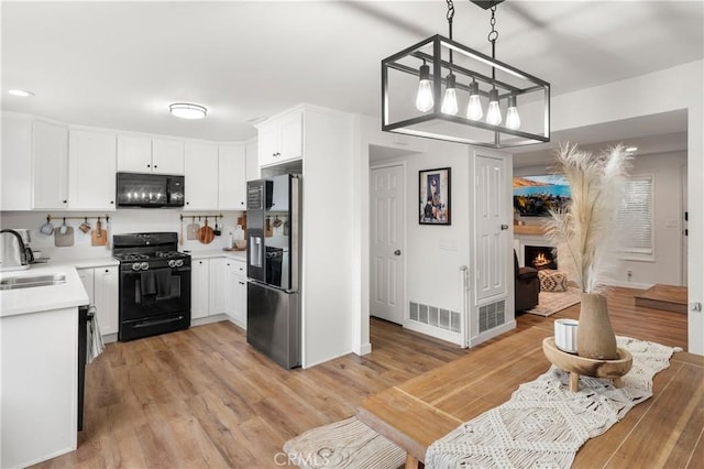 kitchen featuring black appliances, light wood-style flooring, a sink, a warm lit fireplace, and light countertops