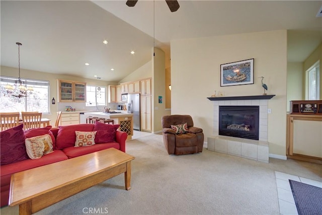 living room with ceiling fan with notable chandelier, a fireplace, high vaulted ceiling, and light carpet