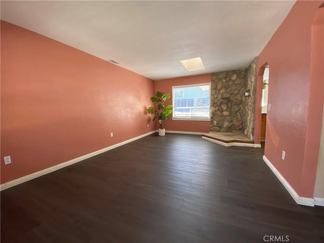 empty room featuring dark wood-type flooring and a skylight