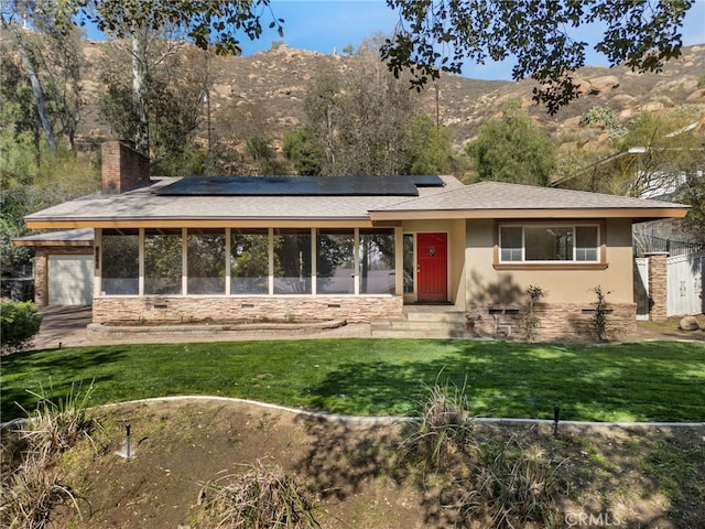 view of front of home featuring a sunroom, entry steps, roof mounted solar panels, and a front yard