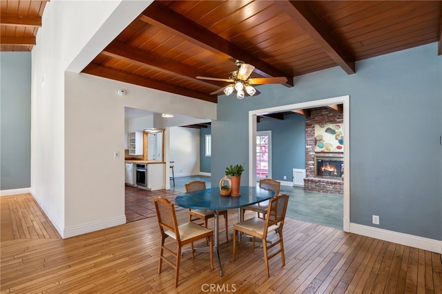 dining space featuring hardwood / wood-style flooring, beam ceiling, wood ceiling, and a brick fireplace