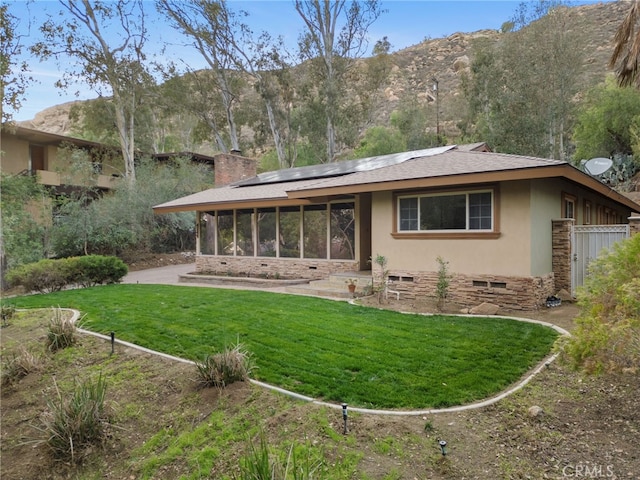 back of house featuring a mountain view, a sunroom, a lawn, and solar panels