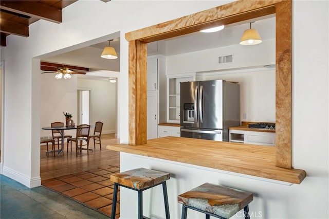 kitchen with butcher block counters, a kitchen breakfast bar, decorative light fixtures, stainless steel fridge, and kitchen peninsula