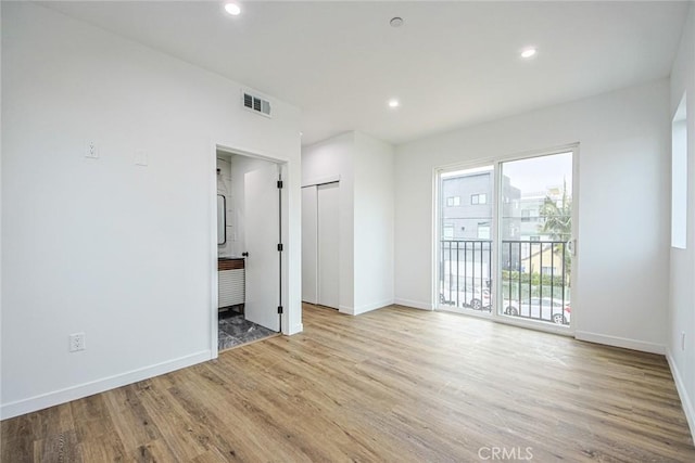 unfurnished room featuring ensuite bathroom, access to exterior, and light wood-type flooring