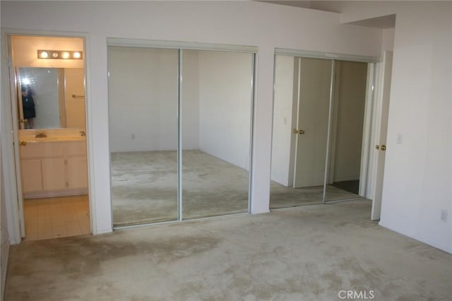 unfurnished bedroom featuring two closets, ensuite bath, and light colored carpet