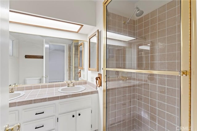 full bathroom featuring toilet, double vanity, a tile shower, and a sink