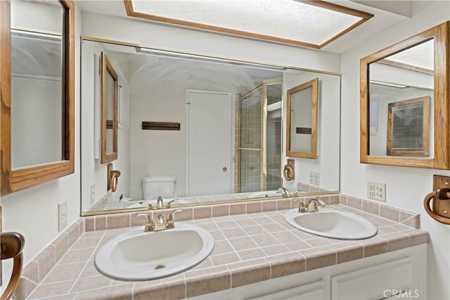 full bath featuring double vanity, a sink, toilet, and a shower with door