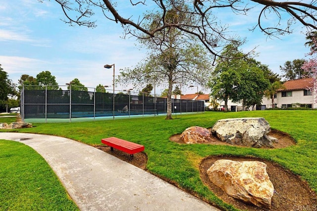 view of home's community featuring tennis court and a yard