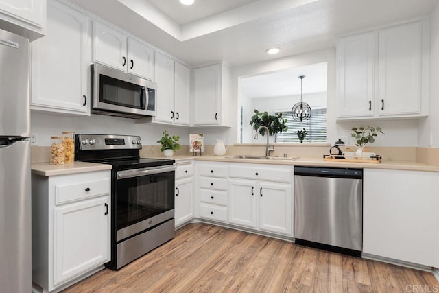 kitchen with appliances with stainless steel finishes, sink, light hardwood / wood-style flooring, white cabinetry, and decorative light fixtures