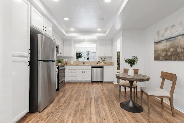 kitchen with light hardwood / wood-style flooring, stainless steel appliances, white cabinets, a raised ceiling, and sink