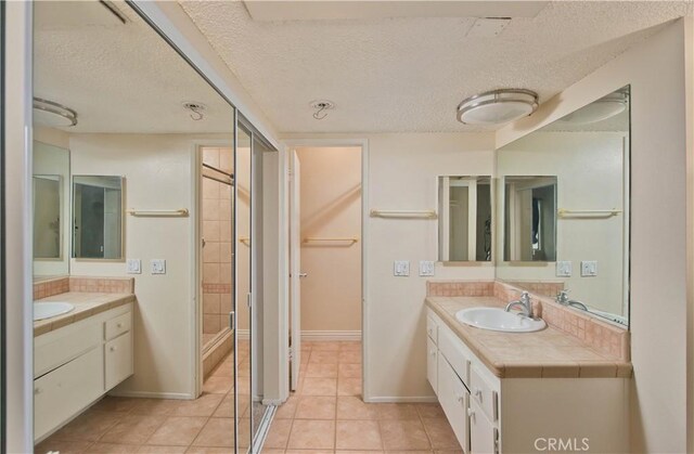 23515 Lyons Ave Unit 228, Valencia, CA 91355 - bathroom featuring a textured ceiling, two vanities, a stall shower, tile patterned floors, and baseboards