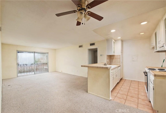 kitchen with a peninsula, tile counters, white cabinets, and gas range gas stove