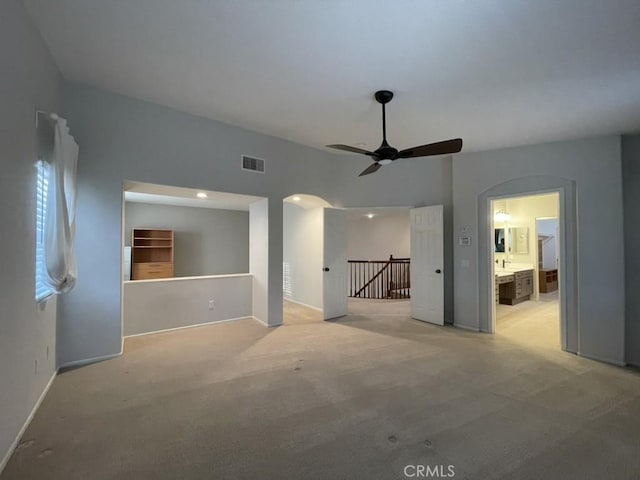 unfurnished living room featuring arched walkways, light colored carpet, visible vents, a ceiling fan, and baseboards