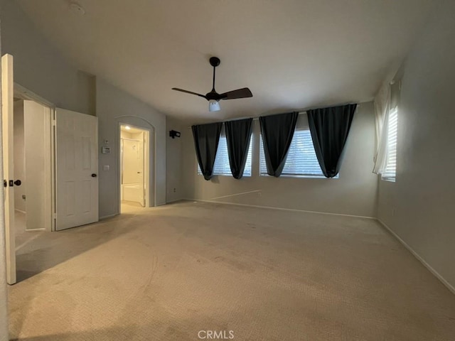 carpeted spare room with a ceiling fan, arched walkways, and baseboards