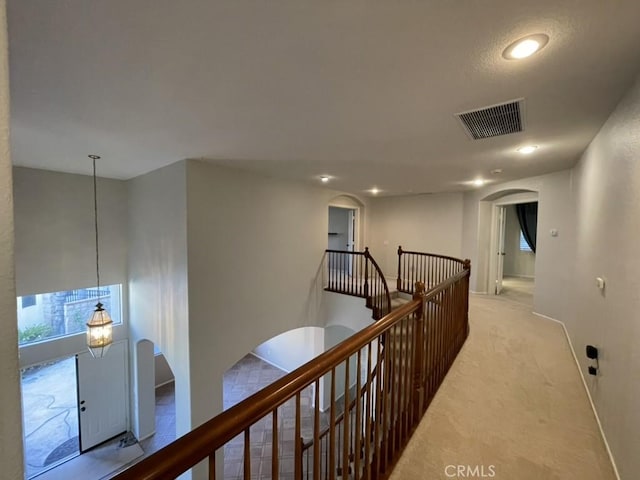 corridor featuring arched walkways, visible vents, light carpet, and an upstairs landing