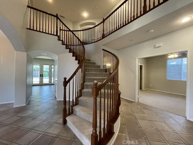 stairway featuring arched walkways, french doors, recessed lighting, a towering ceiling, and baseboards