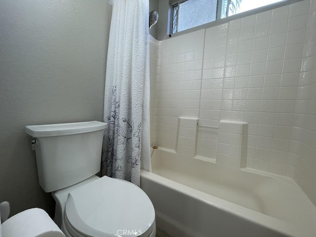 bathroom with a textured wall, toilet, and shower / bath combo with shower curtain