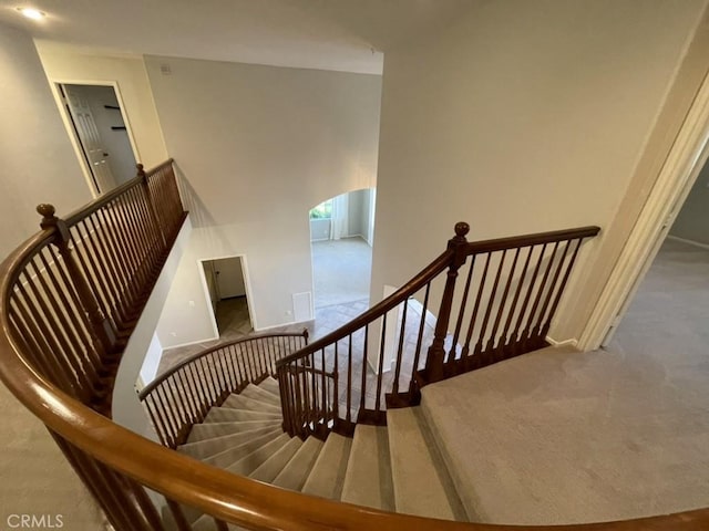 staircase featuring arched walkways, carpet flooring, and baseboards