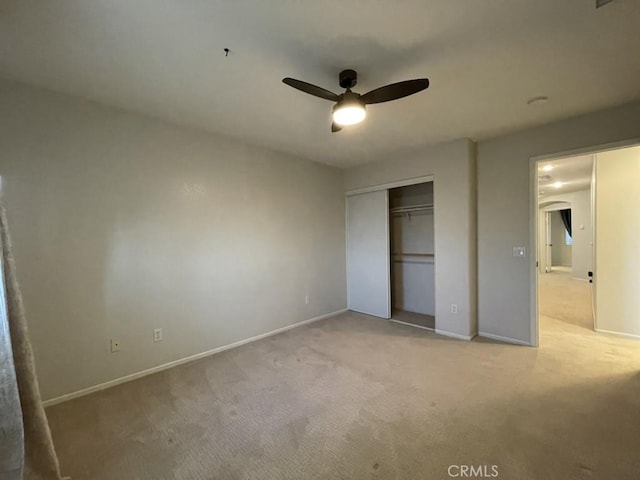 unfurnished bedroom with a ceiling fan, a closet, light carpet, and baseboards