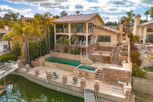 back of house featuring a patio area, a water view, a balcony, and an in ground hot tub