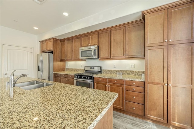 22059 Barrington Way, Saugus, CA 91350 - kitchen featuring appliances with stainless steel finishes, a sink, brown cabinets, light wood-style flooring, and light stone countertops