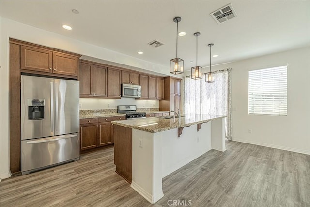 22059 Barrington Way, Saugus, CA 91350 - kitchen featuring stainless steel appliances, wood finished floors, a kitchen bar, light stone countertops, and recessed lighting