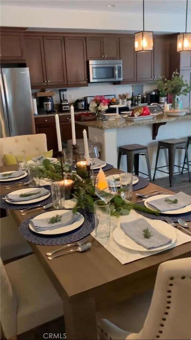 22059 Barrington Way, Saugus, CA 91350 - kitchen featuring appliances with stainless steel finishes, pendant lighting, a kitchen breakfast bar, dark brown cabinetry, and stone countertops