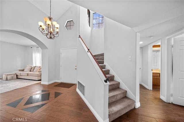 staircase with a notable chandelier, hardwood / wood-style flooring, and high vaulted ceiling