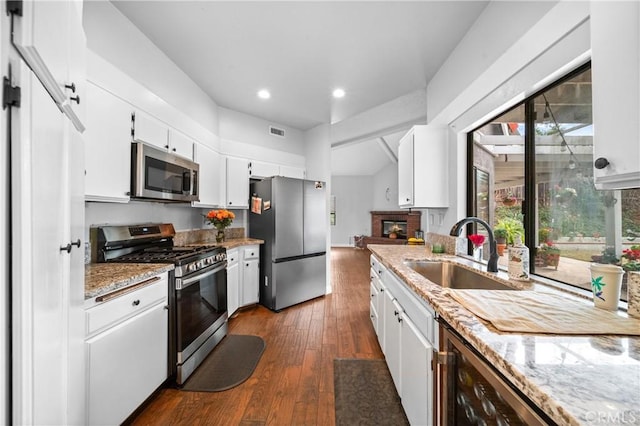 kitchen with appliances with stainless steel finishes, sink, white cabinets, dark hardwood / wood-style flooring, and a brick fireplace