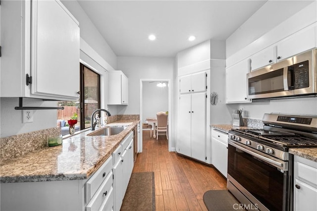 kitchen featuring sink, white cabinetry, light stone counters, stainless steel appliances, and light hardwood / wood-style floors