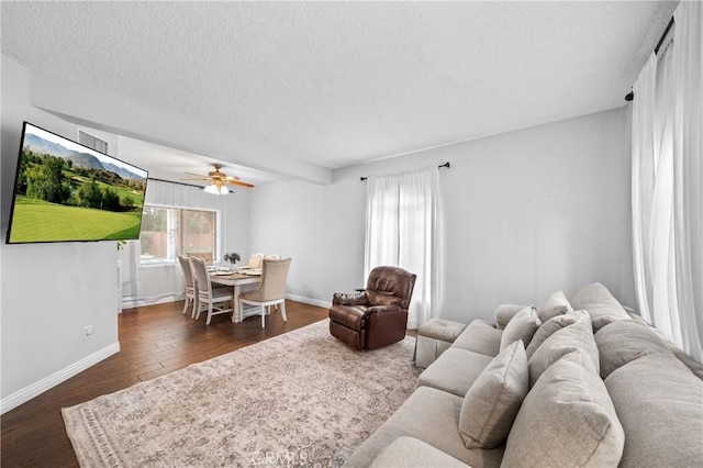 living room with dark hardwood / wood-style flooring, ceiling fan, and a textured ceiling