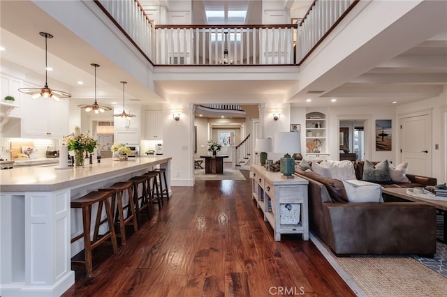 living room featuring a towering ceiling, dark wood-type flooring, built in features, and ceiling fan