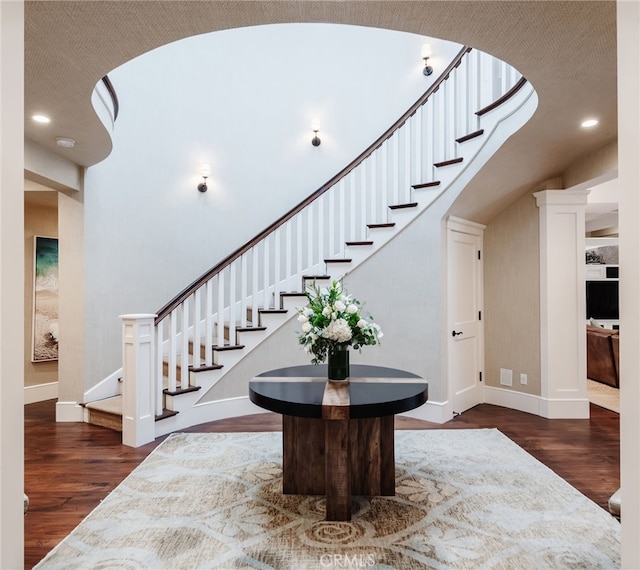 stairway with a towering ceiling, recessed lighting, baseboards, and wood finished floors