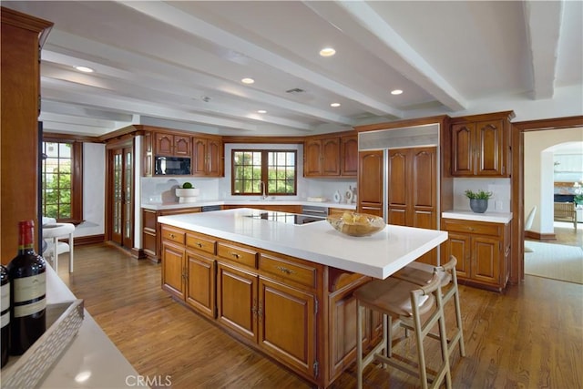 kitchen featuring beam ceiling, a kitchen breakfast bar, wood-type flooring, black appliances, and a kitchen island