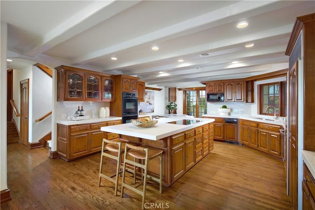 kitchen featuring a breakfast bar, sink, a kitchen island, beamed ceiling, and black appliances