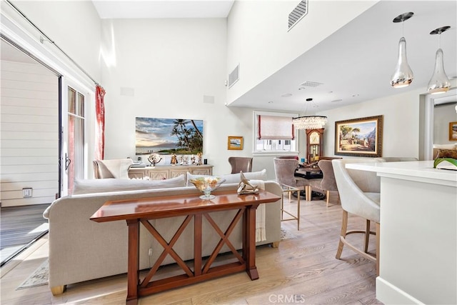 living room with a towering ceiling, light wood finished floors, and visible vents