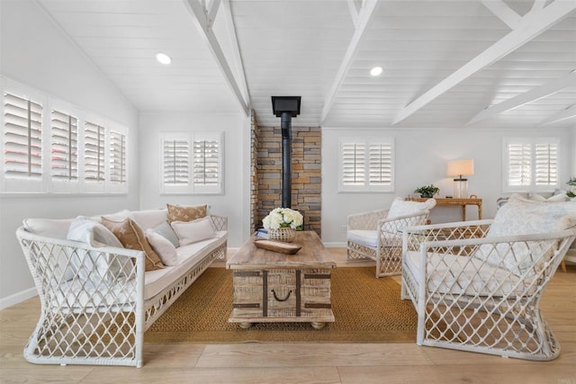 sitting room with a wood stove, lofted ceiling with beams, and a wealth of natural light