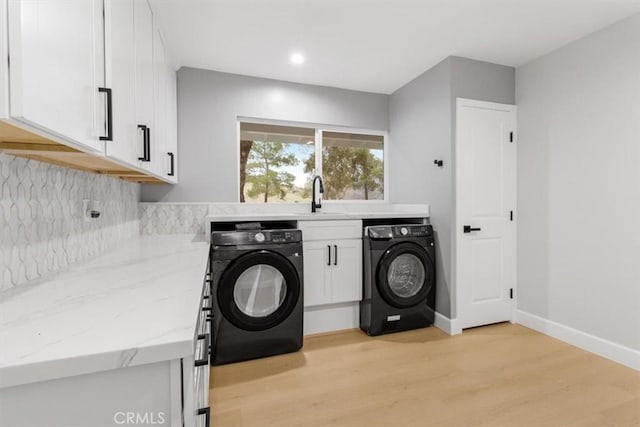 clothes washing area featuring cabinets, sink, washing machine and clothes dryer, and light hardwood / wood-style flooring