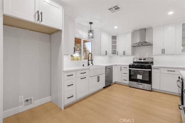 kitchen with white cabinetry, decorative light fixtures, wall chimney exhaust hood, and appliances with stainless steel finishes