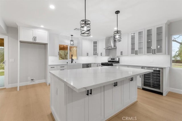 kitchen featuring wall chimney exhaust hood, white cabinetry, a center island, stainless steel appliances, and beverage cooler