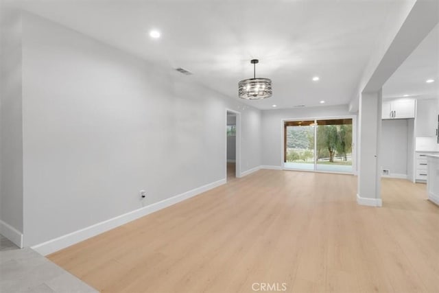 unfurnished living room featuring a notable chandelier and light hardwood / wood-style floors